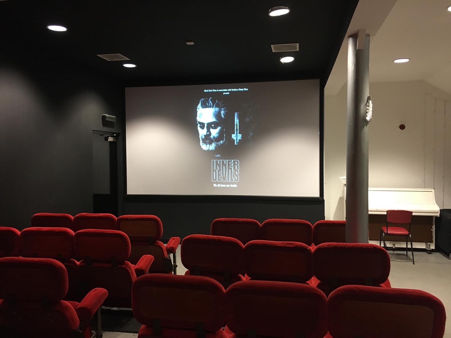 An empty film screening room with a poster of 'Inner Devils' displayed on the screen.